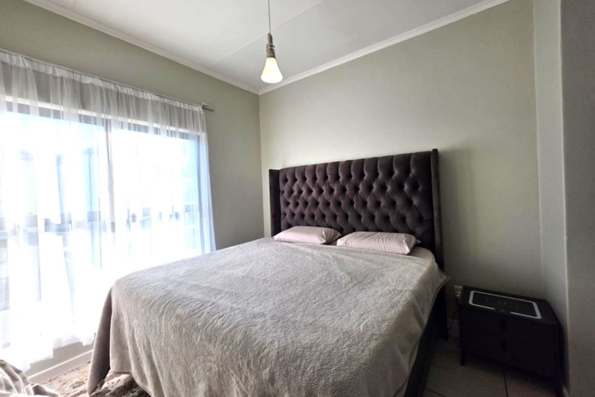 A well-lit bedroom featuring tiled flooring, a sliding glass door providing natural light, and a simple pendant light fixture.