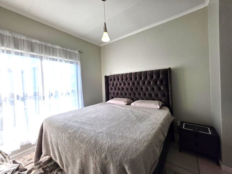 A well-lit bedroom featuring tiled flooring, a sliding glass door providing natural light, and a simple pendant light fixture.