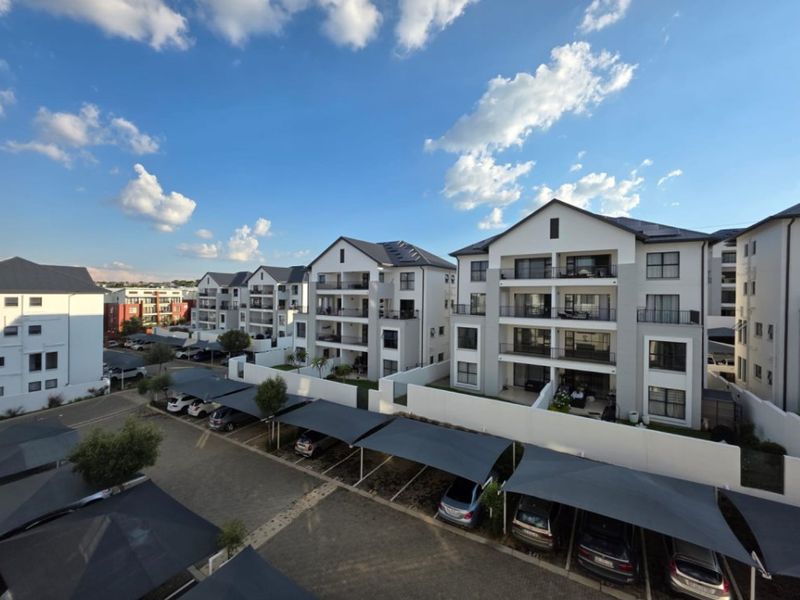 Aerial view of a modern apartment complex featuring multi-story residential buildings, private balconies, and designated covered parking bays within a secure estate.
