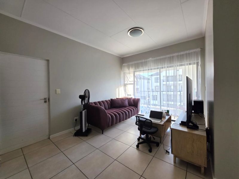 A living room featuring neutral tiled flooring, a ceiling light fixture, and a large sliding glass door providing access to an outdoor balcony area.