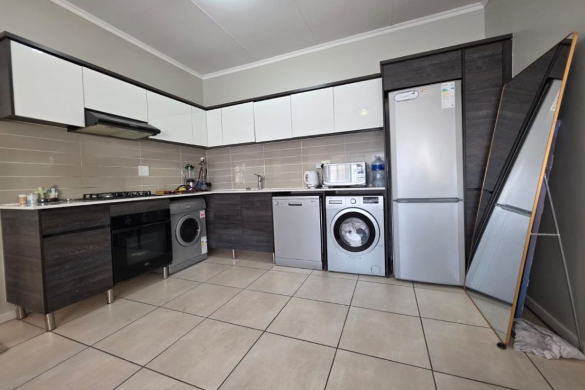 Modern kitchen featuring dark wood-grain and white cabinetry, tiled flooring, integrated appliances, and a neutral tiled backsplash.