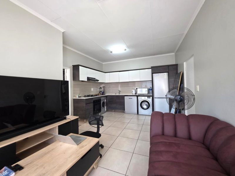 Open-plan living area featuring a modern kitchen with built-in cabinetry, tiled flooring, and integrated appliances, seamlessly flowing into the lounge space.