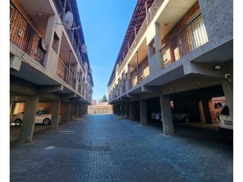 Exterior view of an apartment complex featuring a paved driveway, covered parking area beneath the building, and multiple levels of balconies with metal railings.