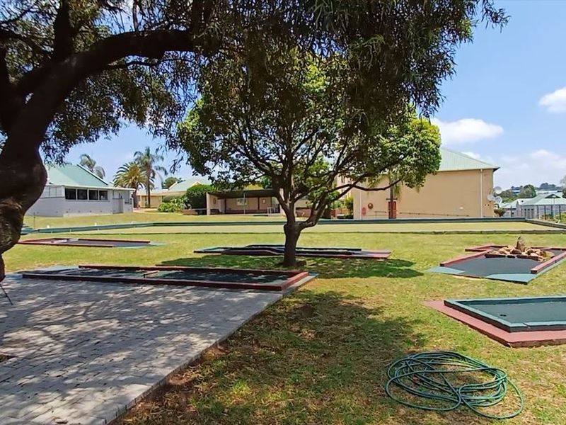 Outdoor miniature golf course facility set within a landscaped communal garden area with mature trees and paved pathways.