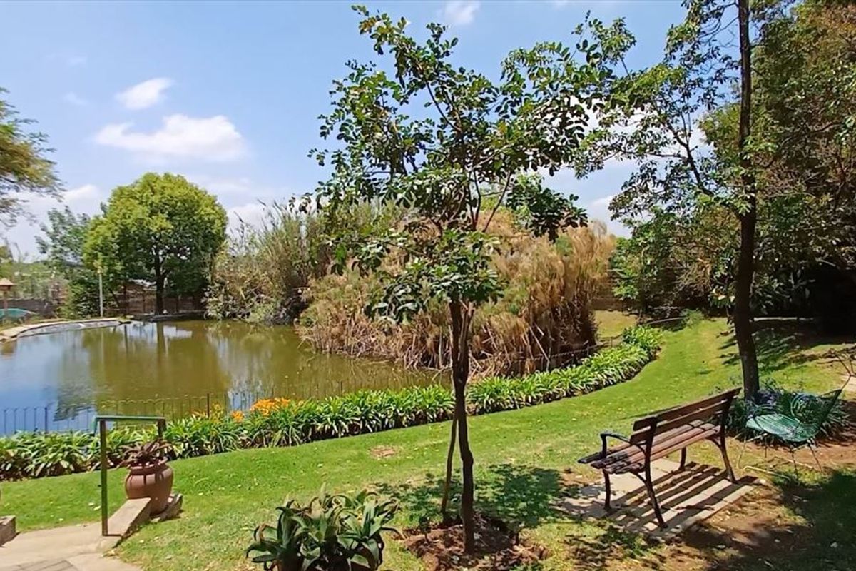 A tranquil garden area featuring a large pond, mature trees, and well-maintained lawn space, providing a peaceful outdoor setting.