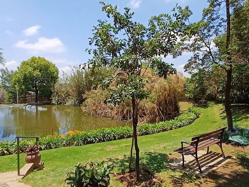 A tranquil garden area featuring a large pond, mature trees, and well-maintained lawn space, providing a peaceful outdoor setting.