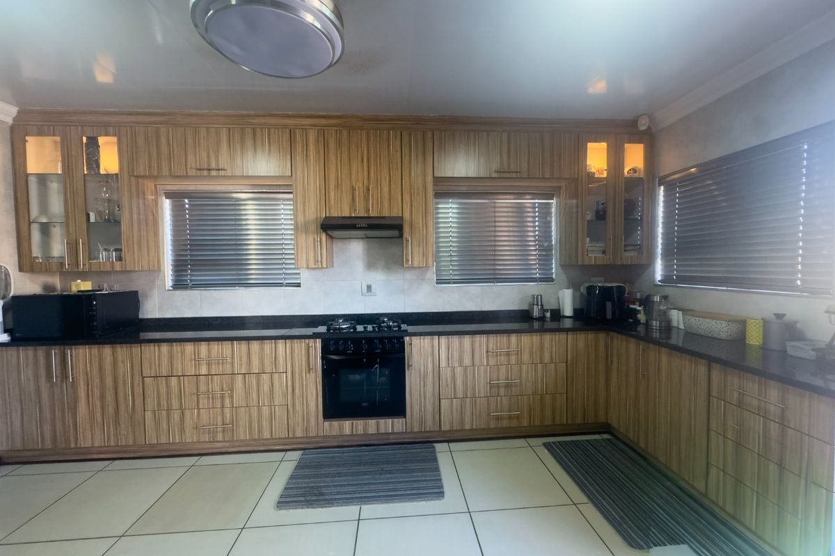 A functional kitchen featuring wood-grain cabinetry, dark granite countertops, a built-in oven, gas hob, and an extractor fan.