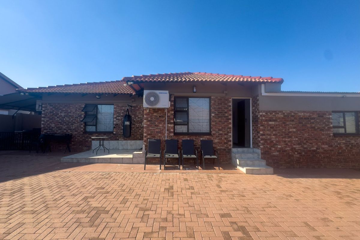 Rear exterior view of a brick townhouse featuring a paved courtyard, tiled roof, and mounted air conditioning unit.
