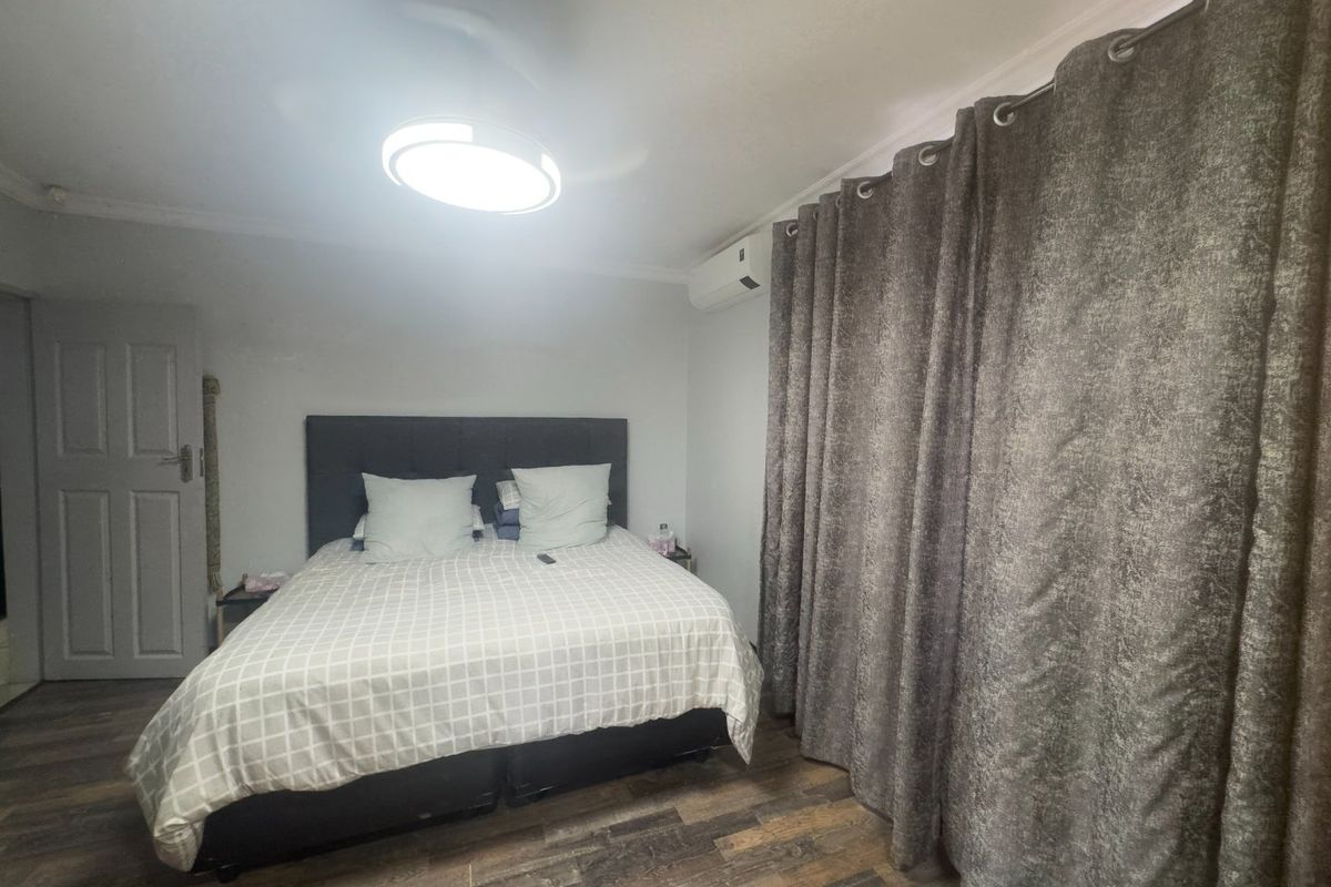 A bedroom featuring wood-look flooring, a wall-mounted air conditioning unit, and a ceiling light fixture.