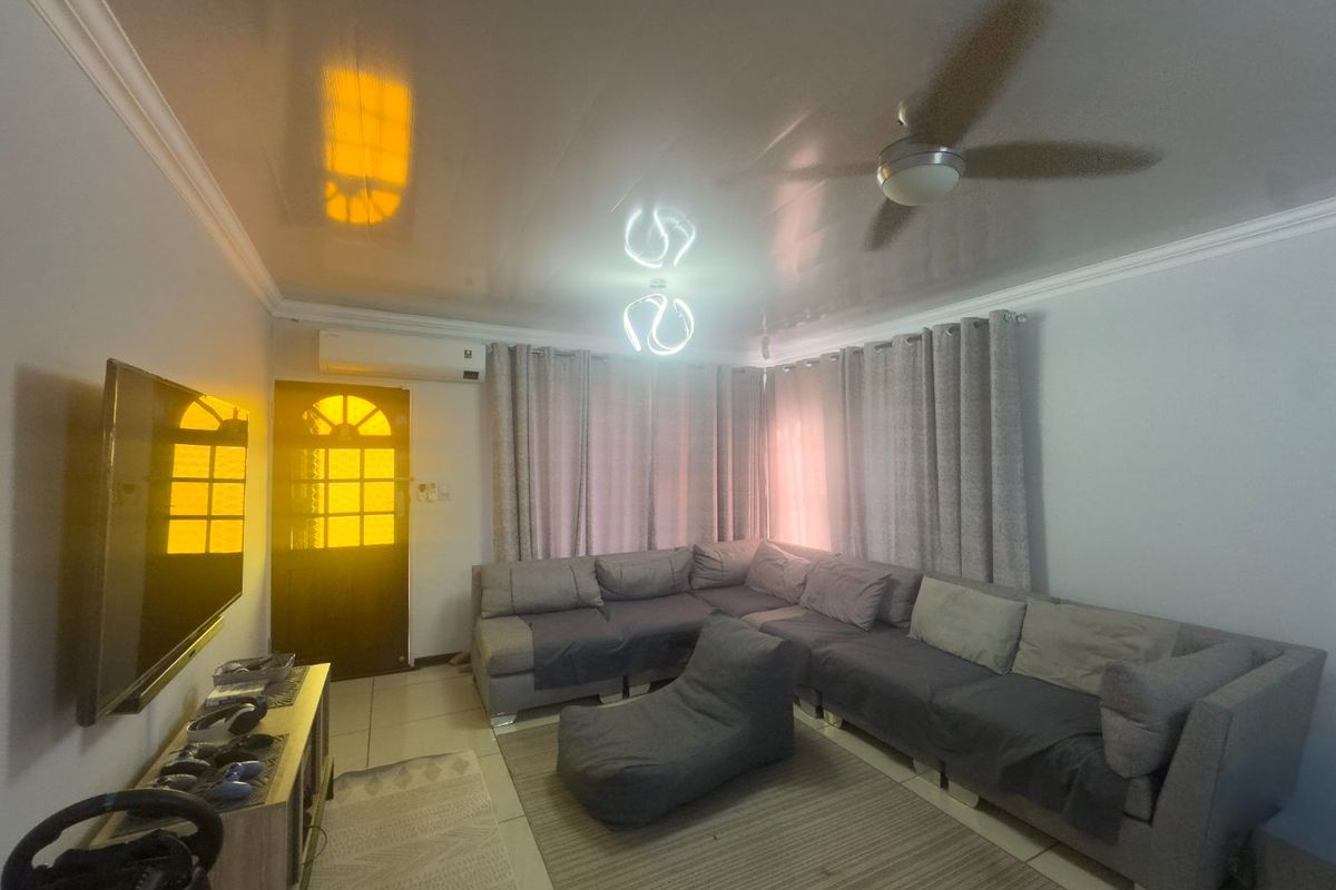 A comfortable living room featuring a glossy ceiling finish, a ceiling fan, and a wall-mounted air conditioning unit.