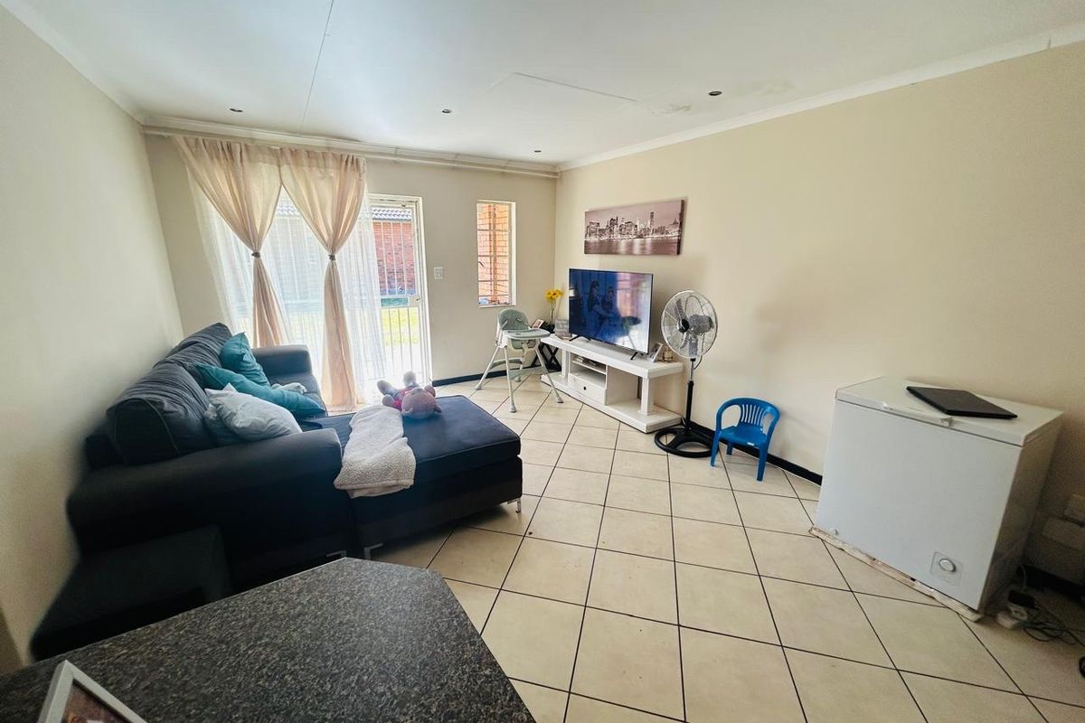 A living room featuring tiled flooring and a sliding glass door leading to the exterior, with visible ceiling water staining.