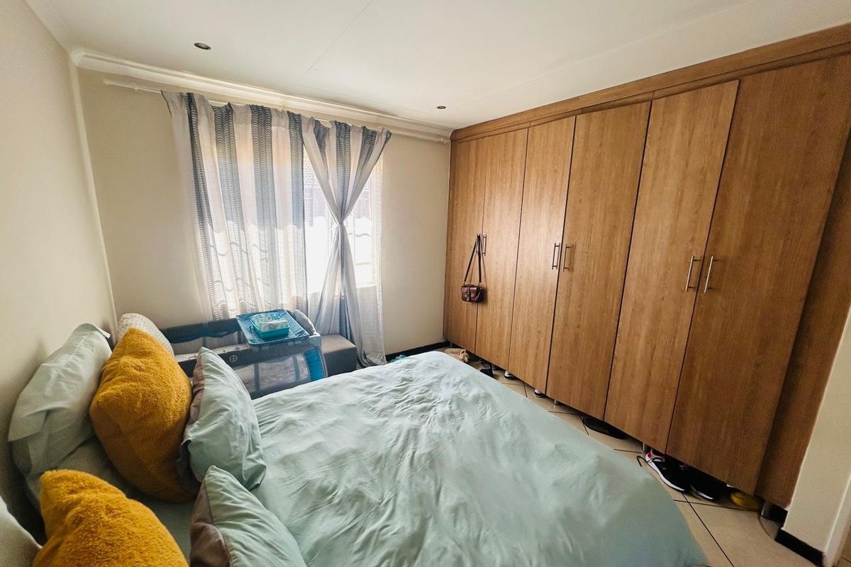 A well-maintained bedroom featuring extensive built-in wooden cupboards, tiled flooring, and recessed ceiling lighting, providing ample storage and a neutral aesthetic.