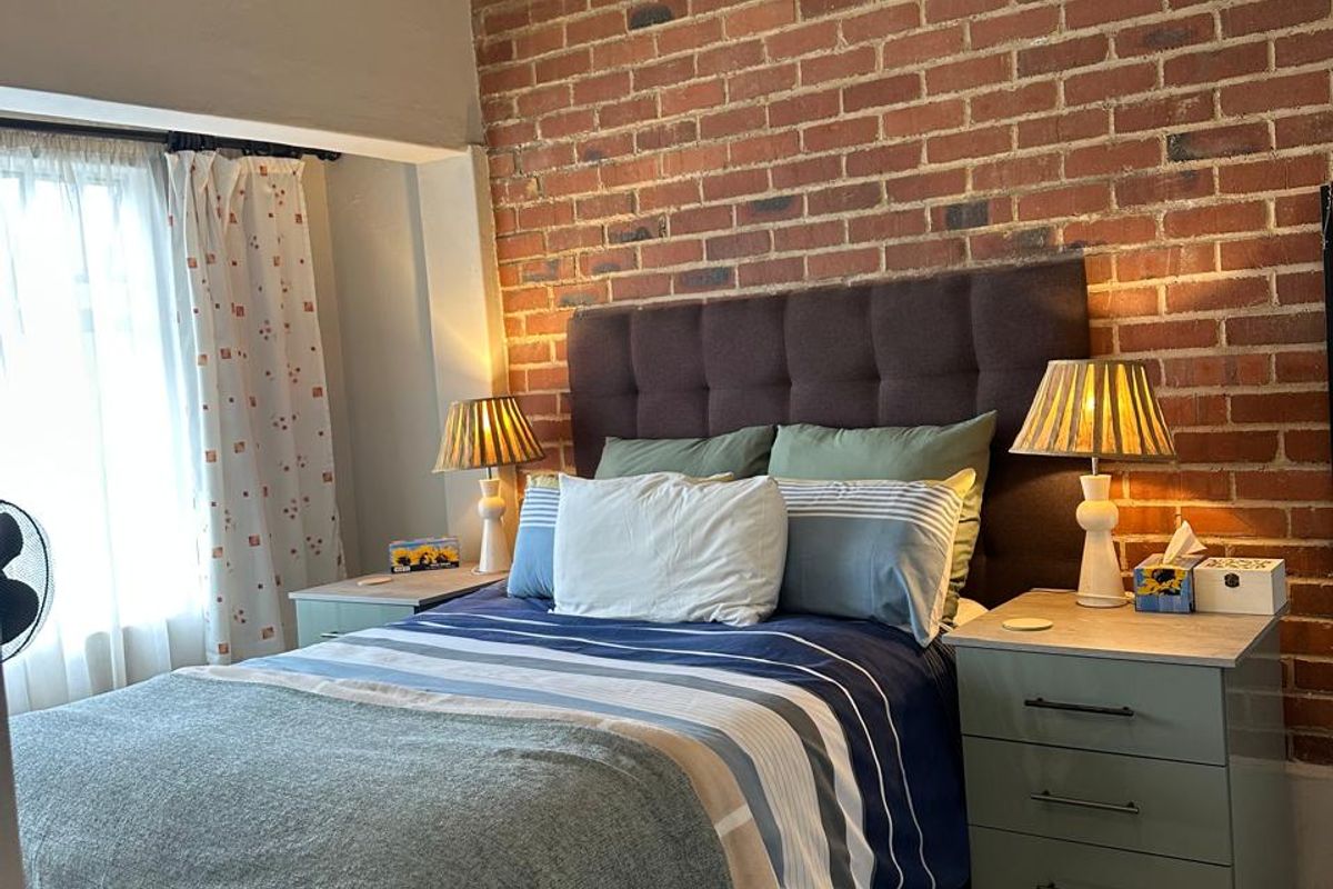 A cozy bedroom featuring a prominent exposed brick feature wall and a high vaulted ceiling, creating a warm and character-filled sleeping space.