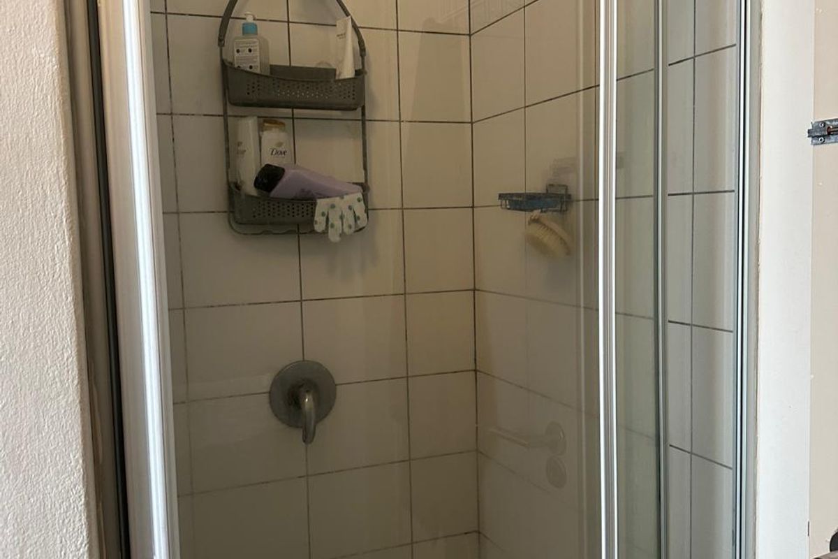 A functional shower stall featuring a glass enclosure, chrome mixer tap, and white ceramic wall tiling.
