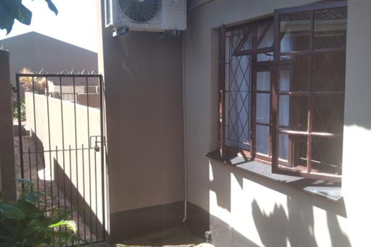 Rear exterior view of the townhouse featuring a paved walkway, security gate, and wall-mounted air conditioning unit.