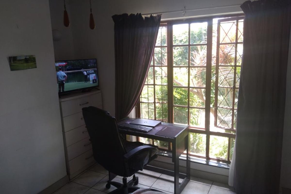 A bedroom featuring tiled flooring and a large window with security bars, currently utilized as a home office space.