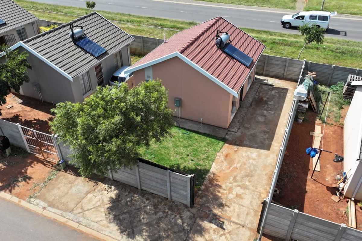 Aerial view of a residential property featuring a tiled roof with a solar water heater, concrete driveway, and enclosed garden area.