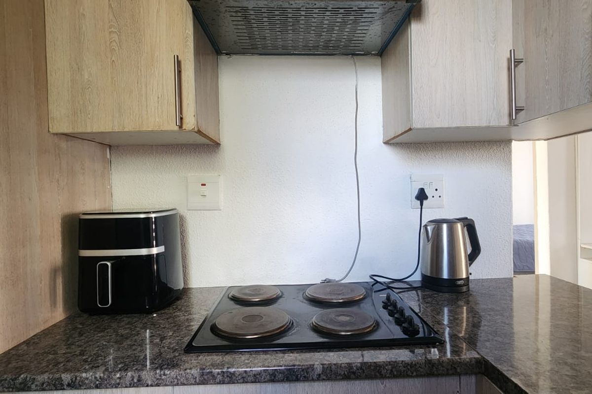 A compact kitchen area featuring laminate cabinetry, granite countertops, and a built-in electric hob with an overhead extractor fan.
