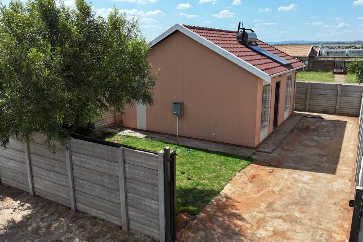 Rear view of the house featuring a solar water heater, tiled roof, and a private garden enclosed by precast concrete boundary walls.