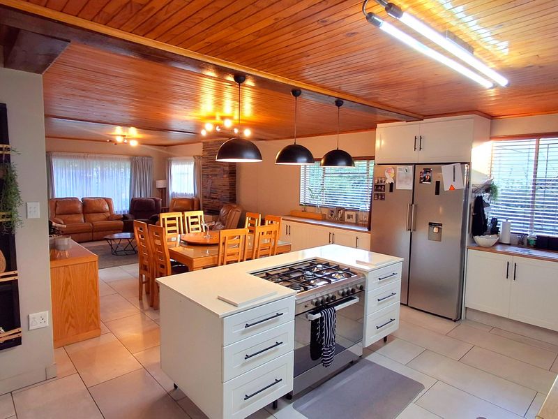 Spacious open-plan kitchen and dining area featuring a central island with gas hob, timber ceilings, and modern tiled flooring throughout.