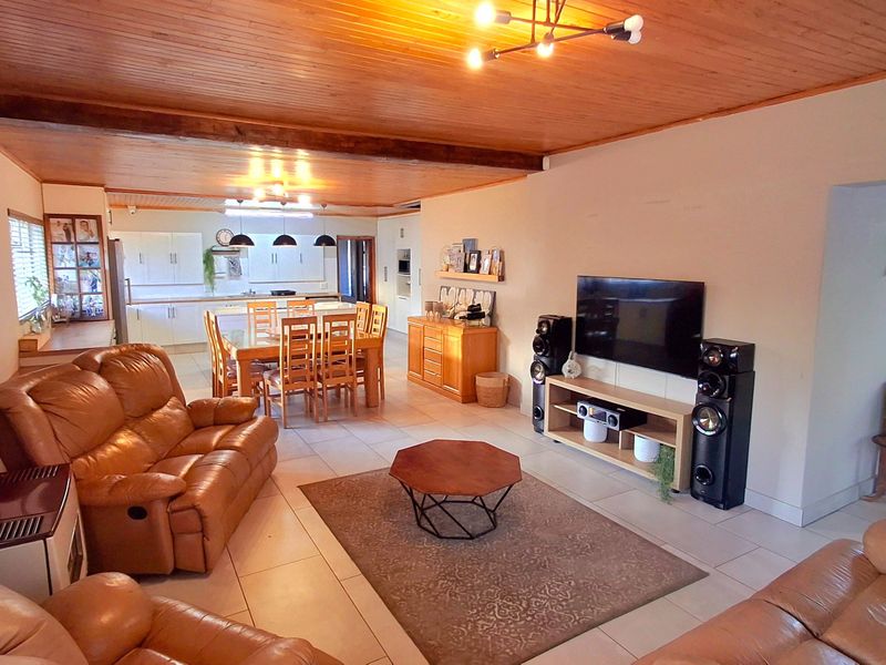 Spacious open-plan living and dining area featuring a stone feature wall, timber ceiling, and a functional kitchen with island bench and ample cabinetry.