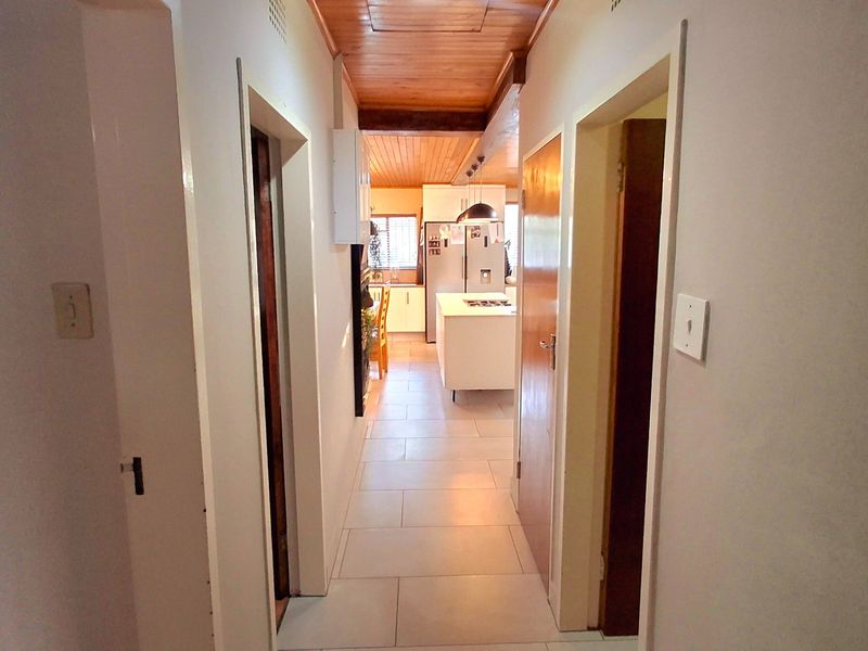 A central hallway with timber ceiling and tiled flooring, providing direct access to the open-plan kitchen area.