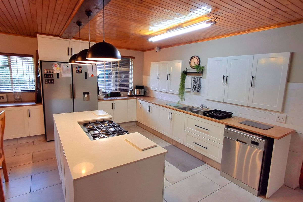 A well-appointed kitchen featuring a central island with a gas hob, ample white cabinetry, timber ceiling finishes, and modern tiled flooring.