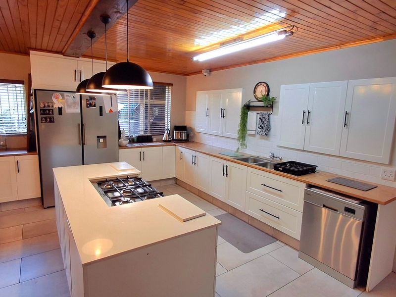 A well-appointed kitchen featuring a central island with a gas hob, ample white cabinetry, timber ceiling finishes, and modern tiled flooring.