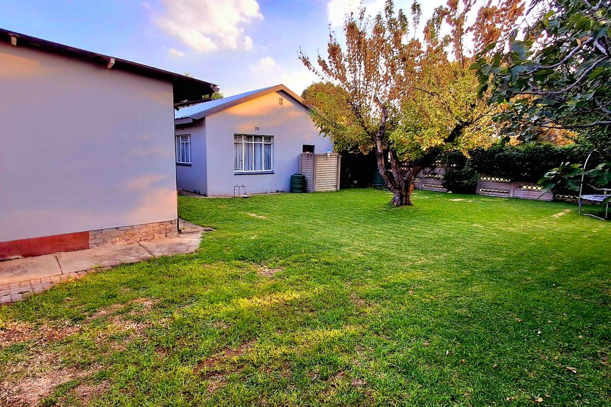 A spacious rear garden featuring a well-maintained lawn, mature trees, and concrete paving, providing a private outdoor area for the property.
