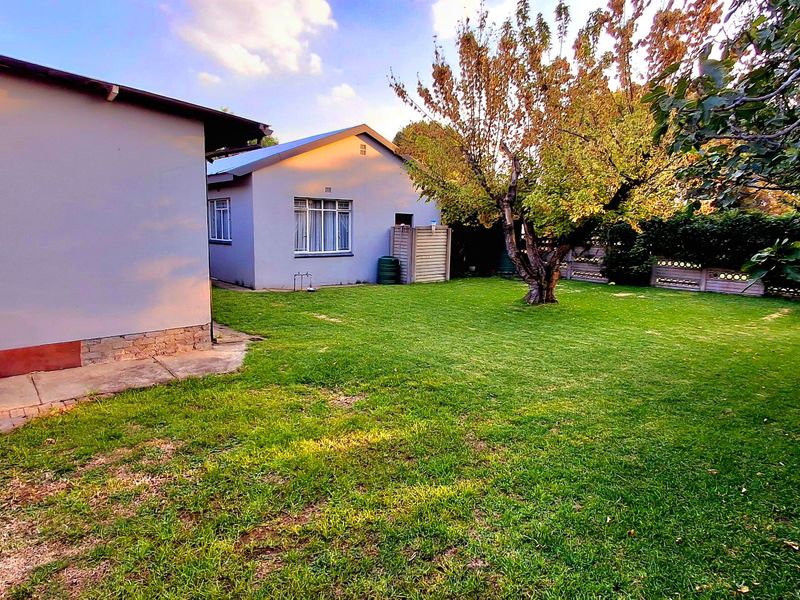 A spacious rear garden featuring a well-maintained lawn, mature trees, and concrete paving, providing a private outdoor area for the property.