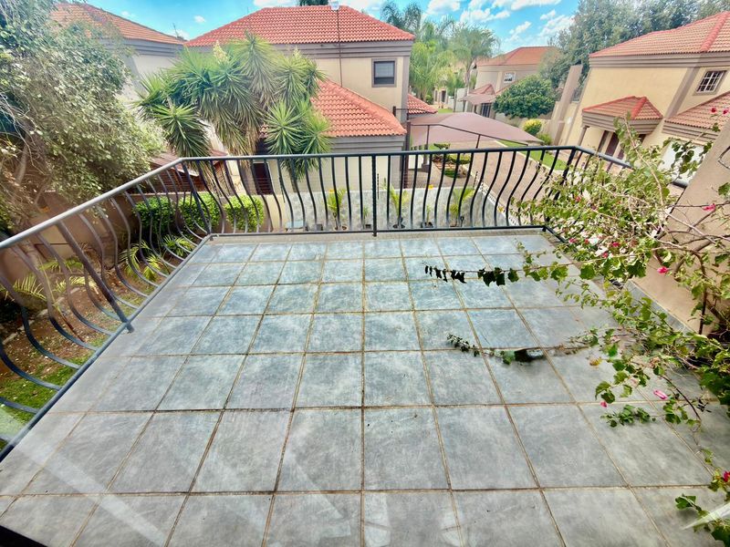 An elevated balcony featuring tiled flooring and a metal balustrade, overlooking the surrounding townhouse complex garden area.
