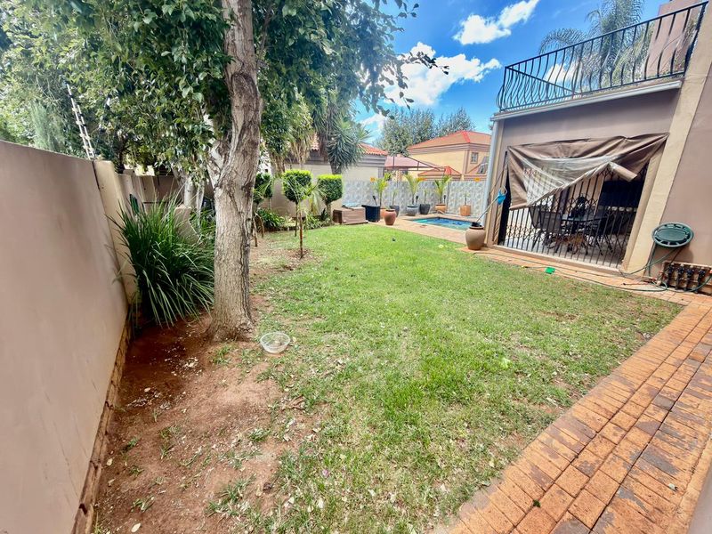 Private rear garden featuring a lawn, paved patio area, and a swimming pool, complemented by an upper-level balcony with wrought iron railings.