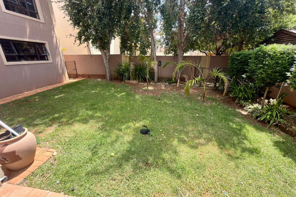 A private rear garden featuring a lawn, established trees, and a paved patio area adjacent to the townhouse structure.