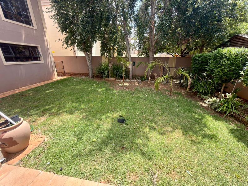 A private rear garden featuring a lawn, established trees, and a paved patio area adjacent to the townhouse structure.