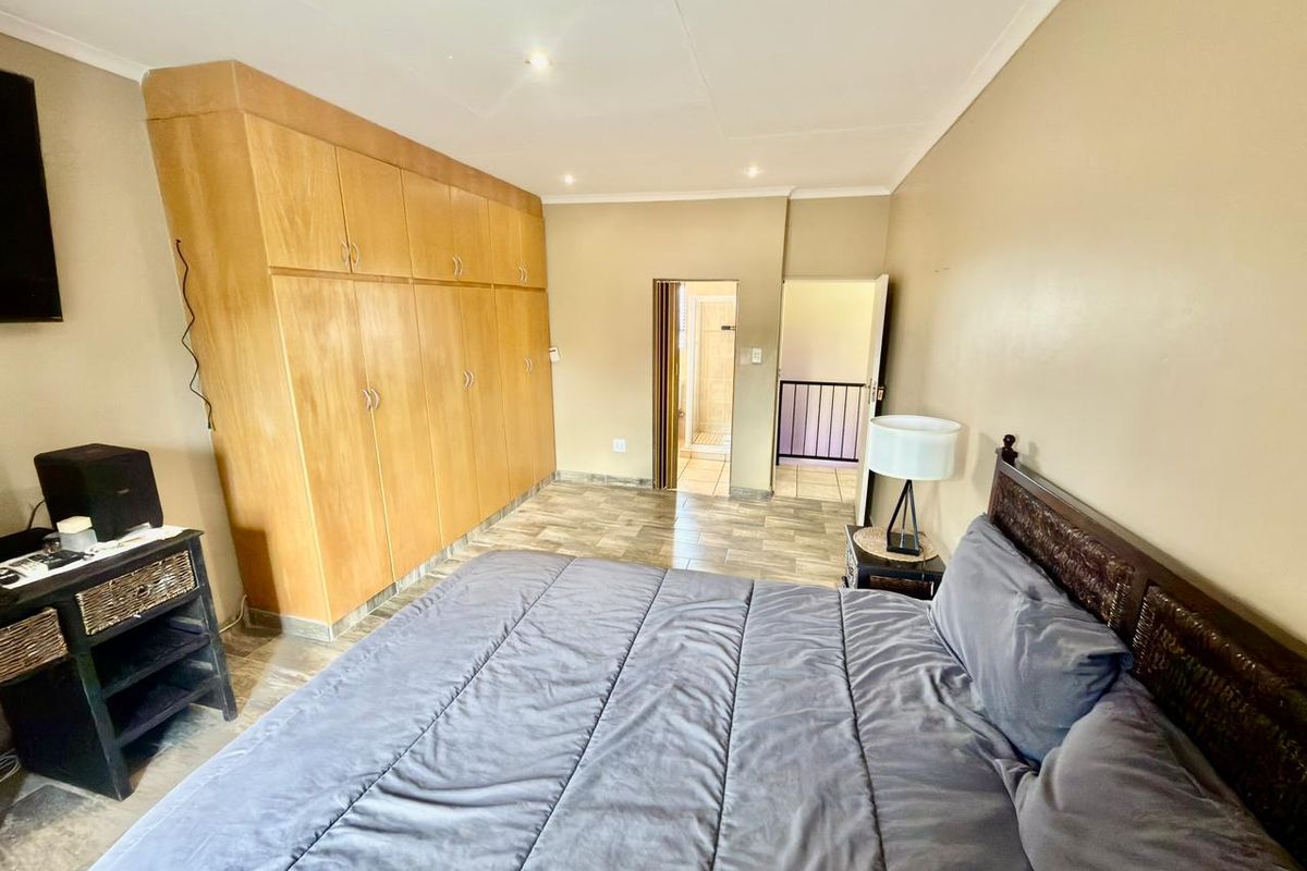 Spacious bedroom featuring built-in wooden cupboards, tiled flooring, recessed lighting, and direct access to an en-suite bathroom.