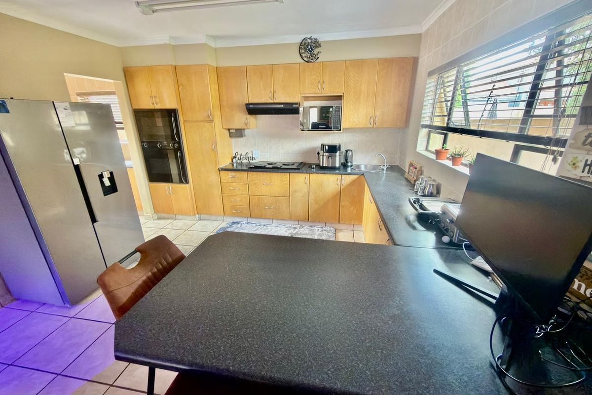 A functional kitchen featuring light wood cabinetry, dark laminate countertops, built-in oven, hob, and tiled flooring with a breakfast bar area.