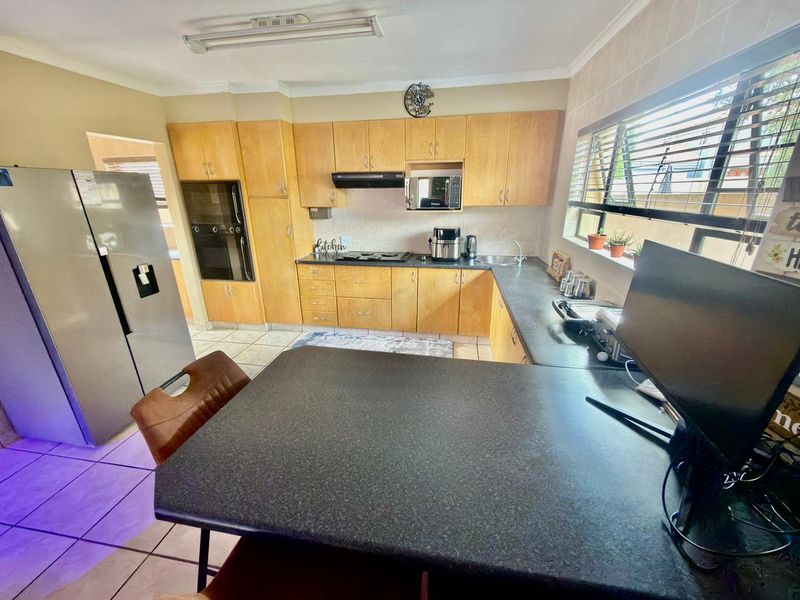 A functional kitchen featuring light wood cabinetry, dark laminate countertops, built-in oven, hob, and tiled flooring with a breakfast bar area.