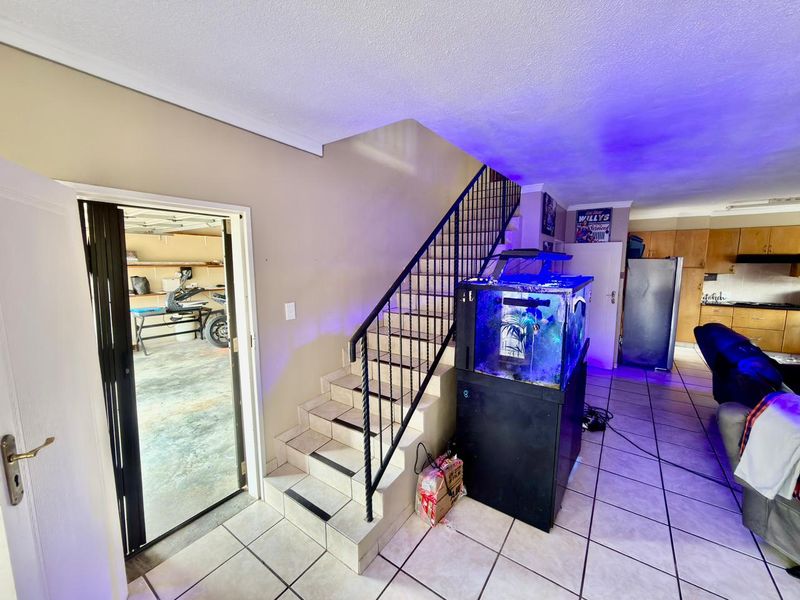 Open plan living area featuring a tiled staircase with metal balustrade, connecting to the kitchen and providing direct internal access to the garage.