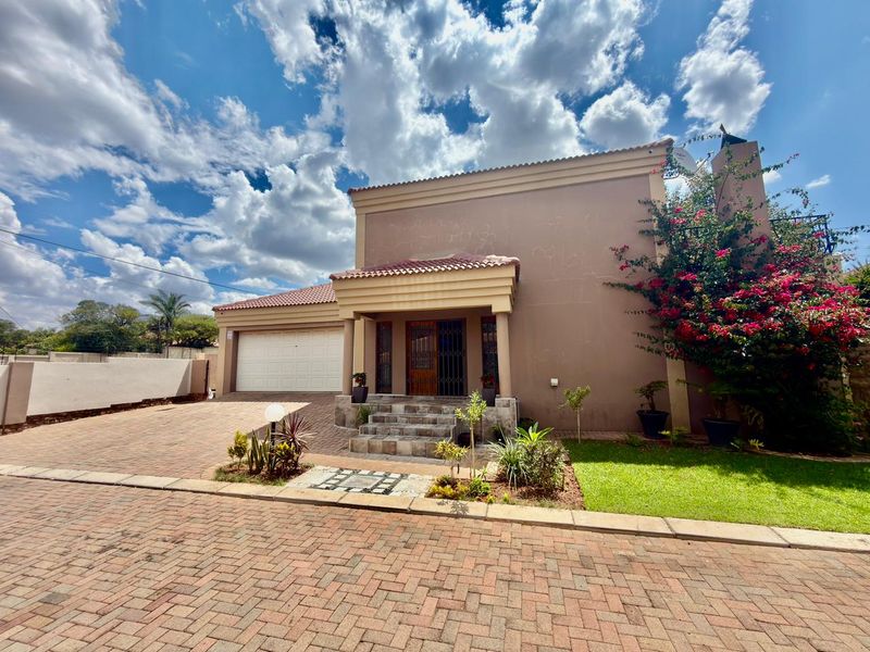 Front elevation of a townhouse featuring a paved driveway, double garage, covered entrance porch with tiled steps, and a well-maintained front garden.