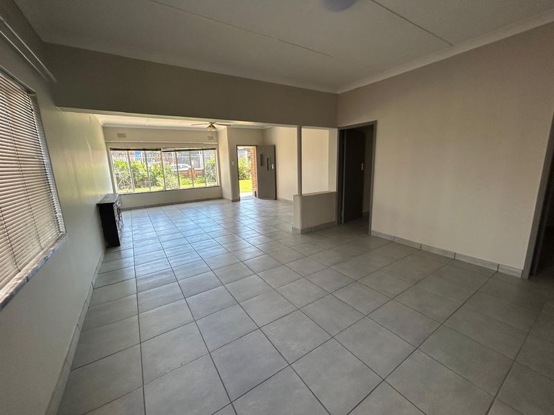 Spacious open-plan living area featuring neutral tiled flooring, large windows for natural light, and direct access to the exterior.