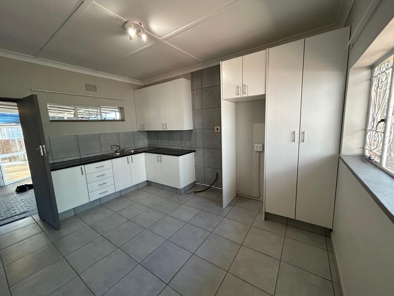 A clean, empty kitchen featuring white built-in cabinetry, dark countertops, tiled splashbacks, and tiled flooring, ready for appliance installation.