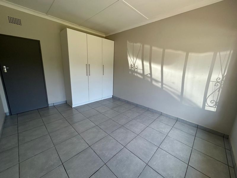 A clean, empty bedroom featuring neutral tiled flooring, a built-in wardrobe, and a security gate on the window.