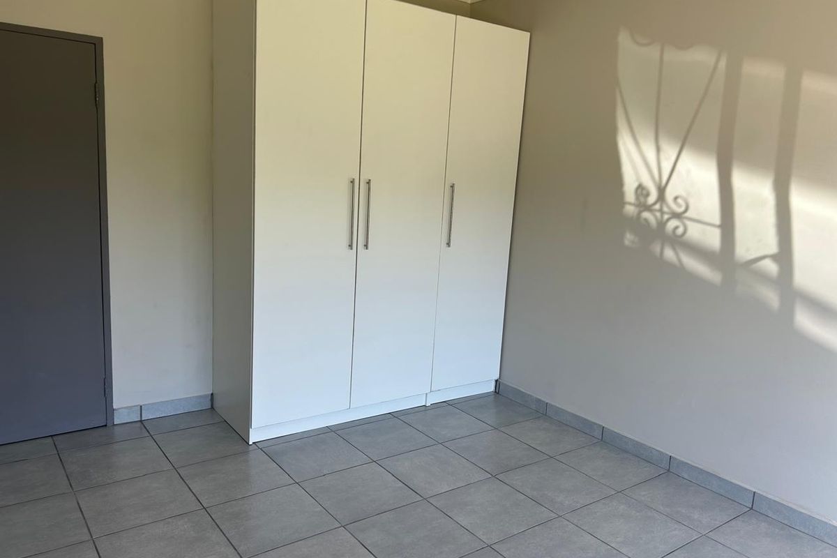 A clean, empty bedroom featuring neutral tiled flooring and a modern white built-in wardrobe.