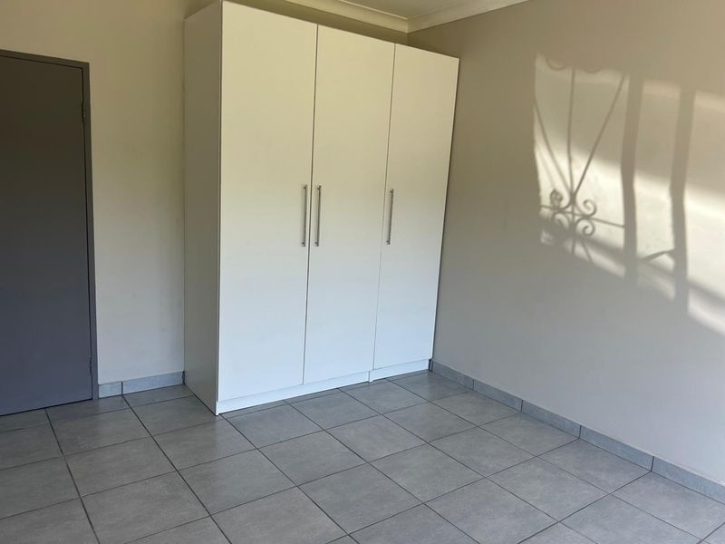 A clean, empty bedroom featuring neutral tiled flooring and a modern white built-in wardrobe.