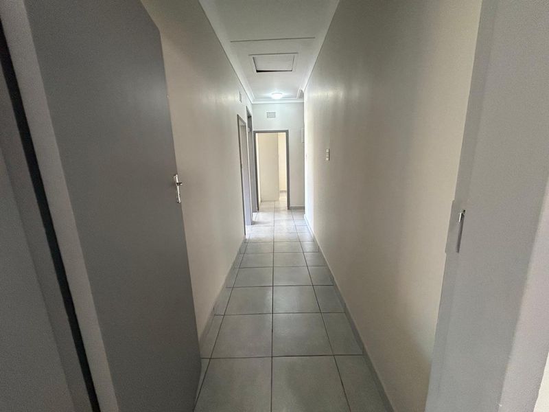 A clean, neutral hallway featuring tiled flooring and access to multiple rooms, providing a functional transition space within the home.