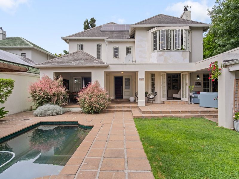 Rear view of the house featuring a tiled patio, swimming pool, and garden area with access through multiple sets of french doors.