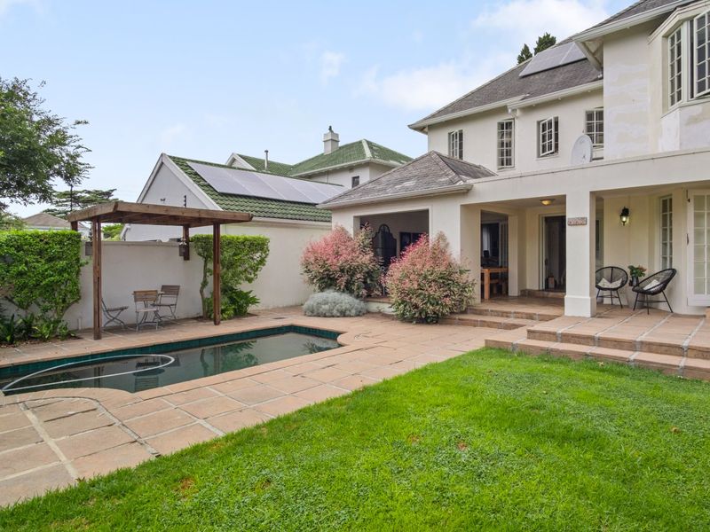 Rear exterior view featuring a swimming pool, paved patio area, covered veranda, and established garden with solar panels installed on the roof.
