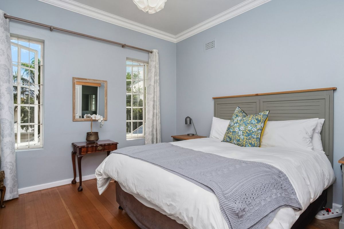 A well-maintained bedroom featuring polished timber flooring, classic cornice detailing, and dual casement windows providing natural light.