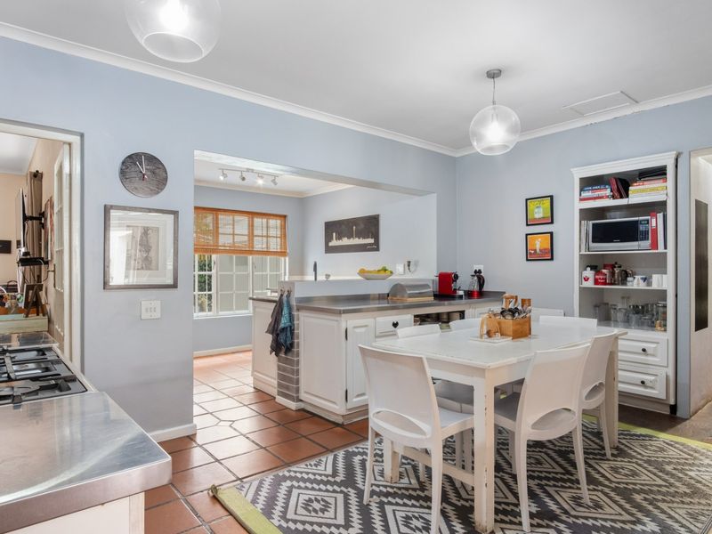 Open-plan kitchen and dining area featuring stainless steel countertops, gas cooktop, terracotta flooring, and built-in cabinetry with integrated shelving.