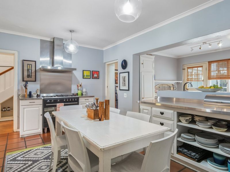 Open-plan kitchen and dining area featuring stainless steel appliances, built-in cabinetry, and terracotta flooring, creating a functional and connected living space.